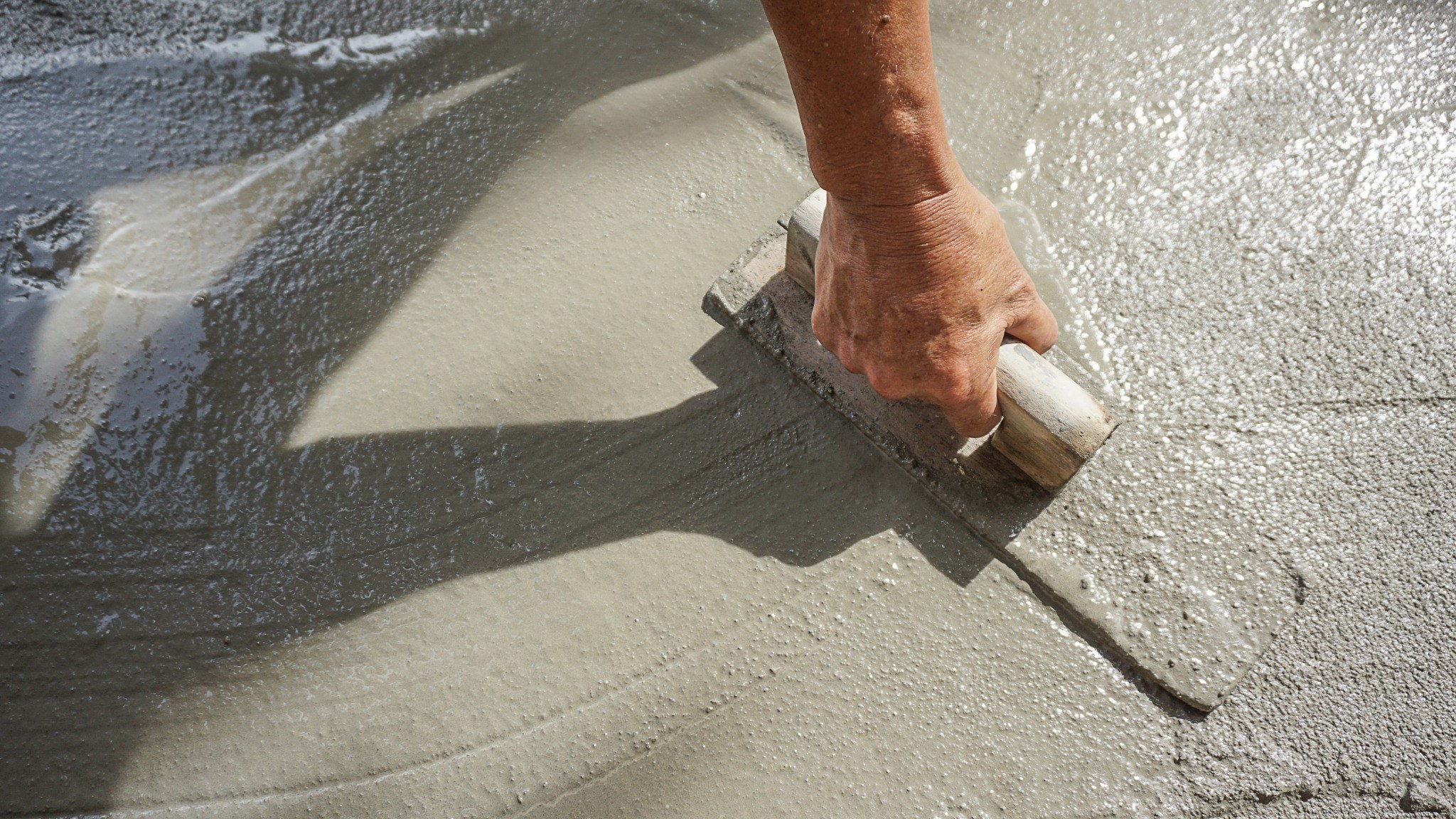 Worker applying wet concrete with a trowel on a residential floor