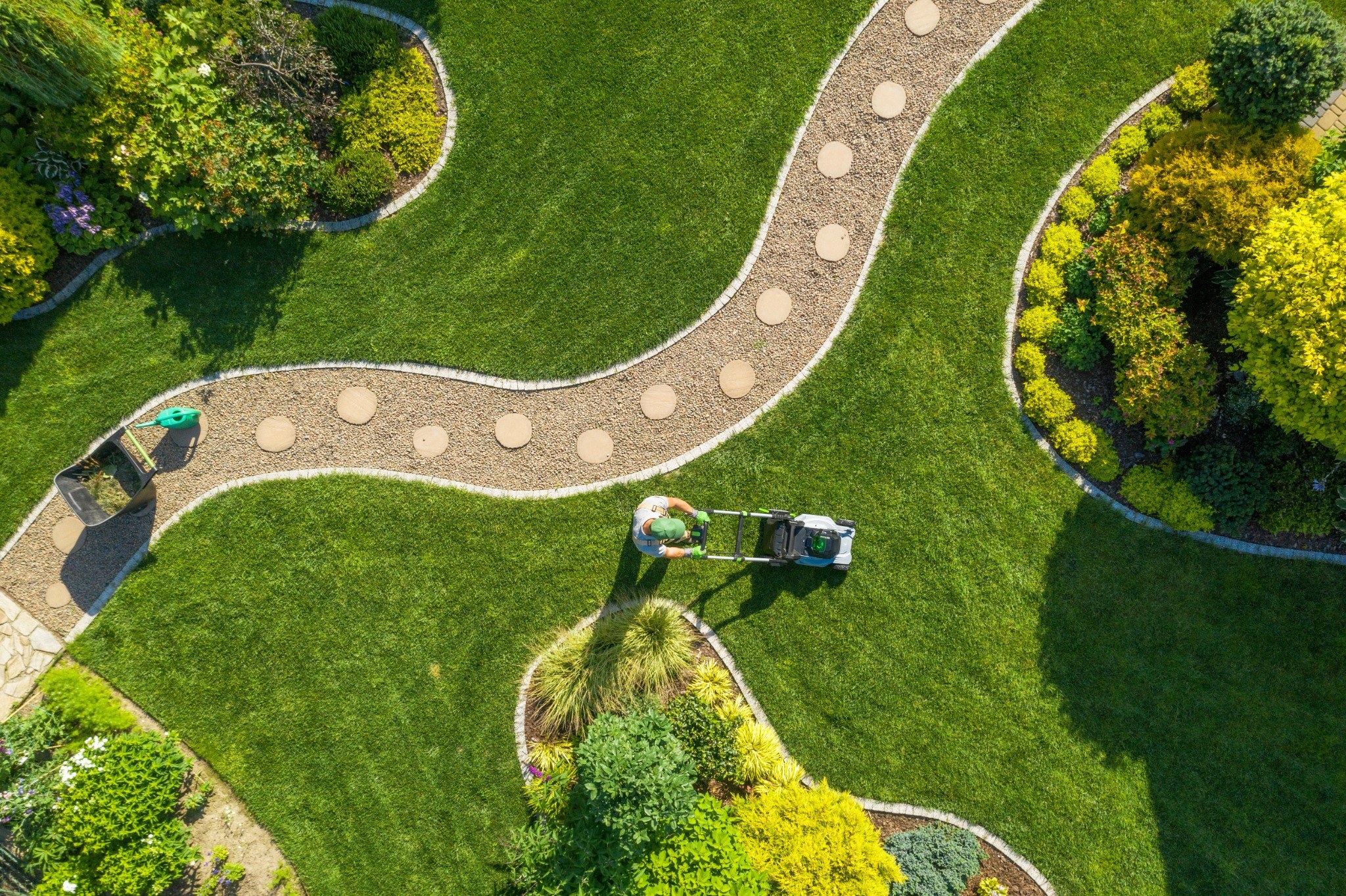 Aerial view of landscaper mowing curved pathway through manicured lawn and garden beds